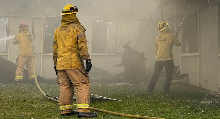 Firefighters in full gear battling a blaze with hoses and smoke in the background