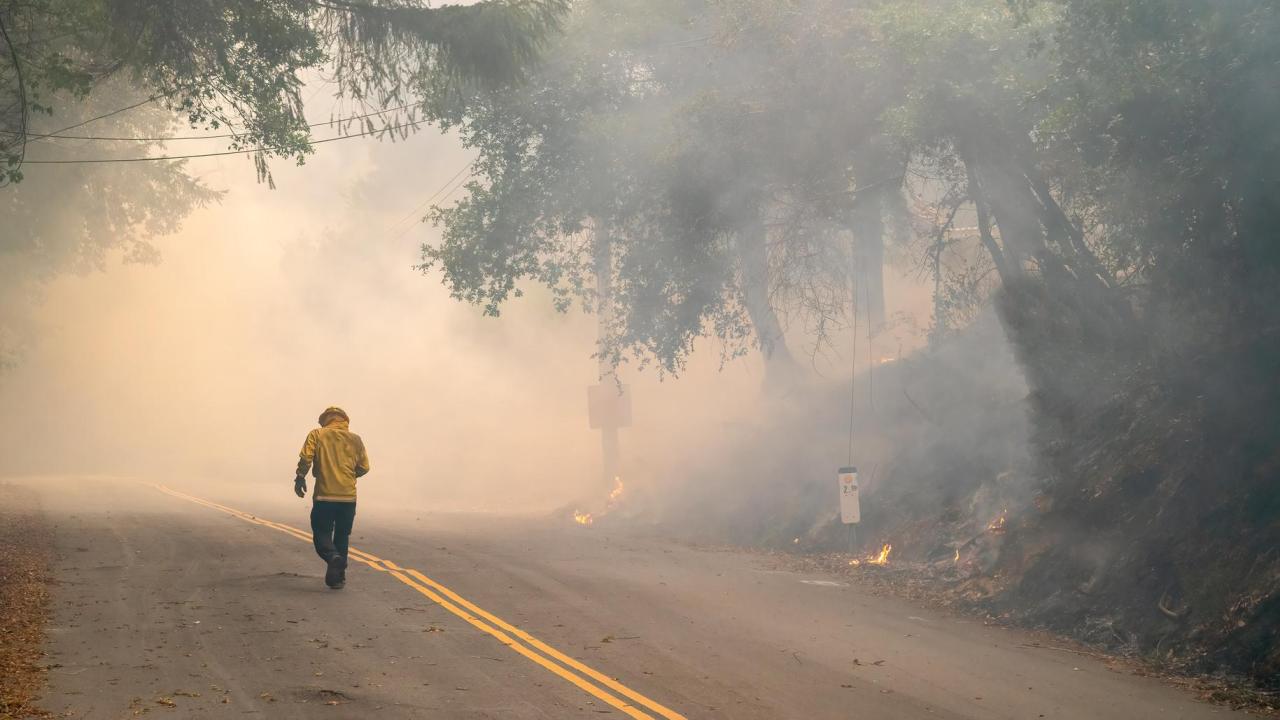 Emergency response to a wildfire: firefighter and flames obscured by heavy smoke on an asphalt road