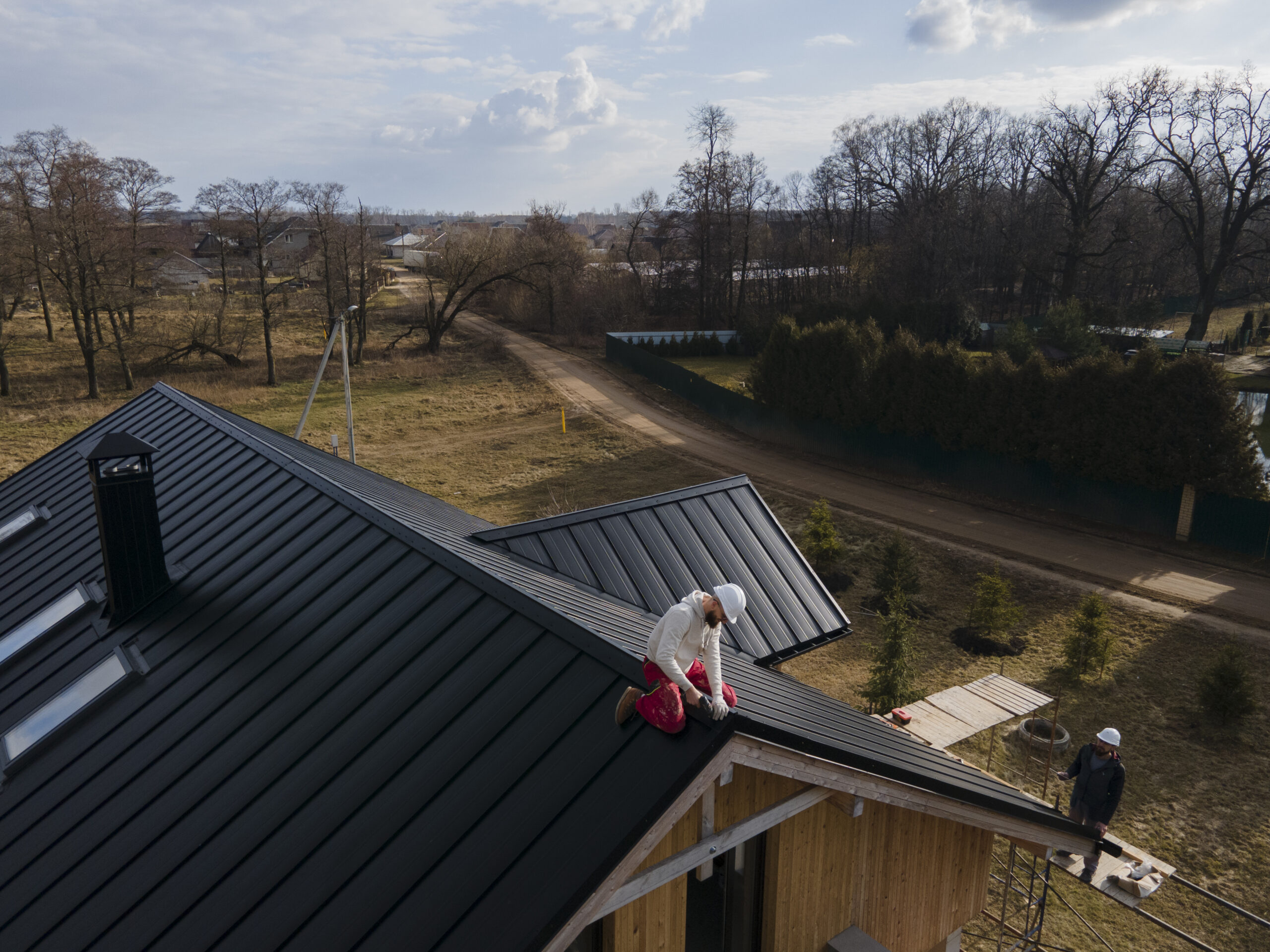 Construction workers fixing black metal roofing on residential home