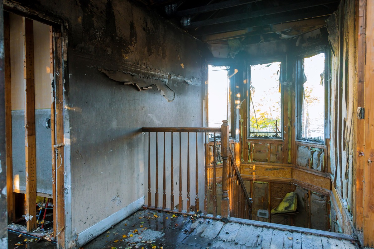 Ruined home interior after a fire, featuring charred walls, water-damaged wooden floors, and a broken window frame, symbolizing devastating property loss