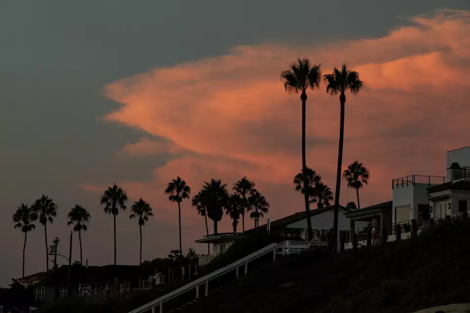 Silhouettes of palm trees and hillside beach houses against a dramatic orange and pink sunset sky